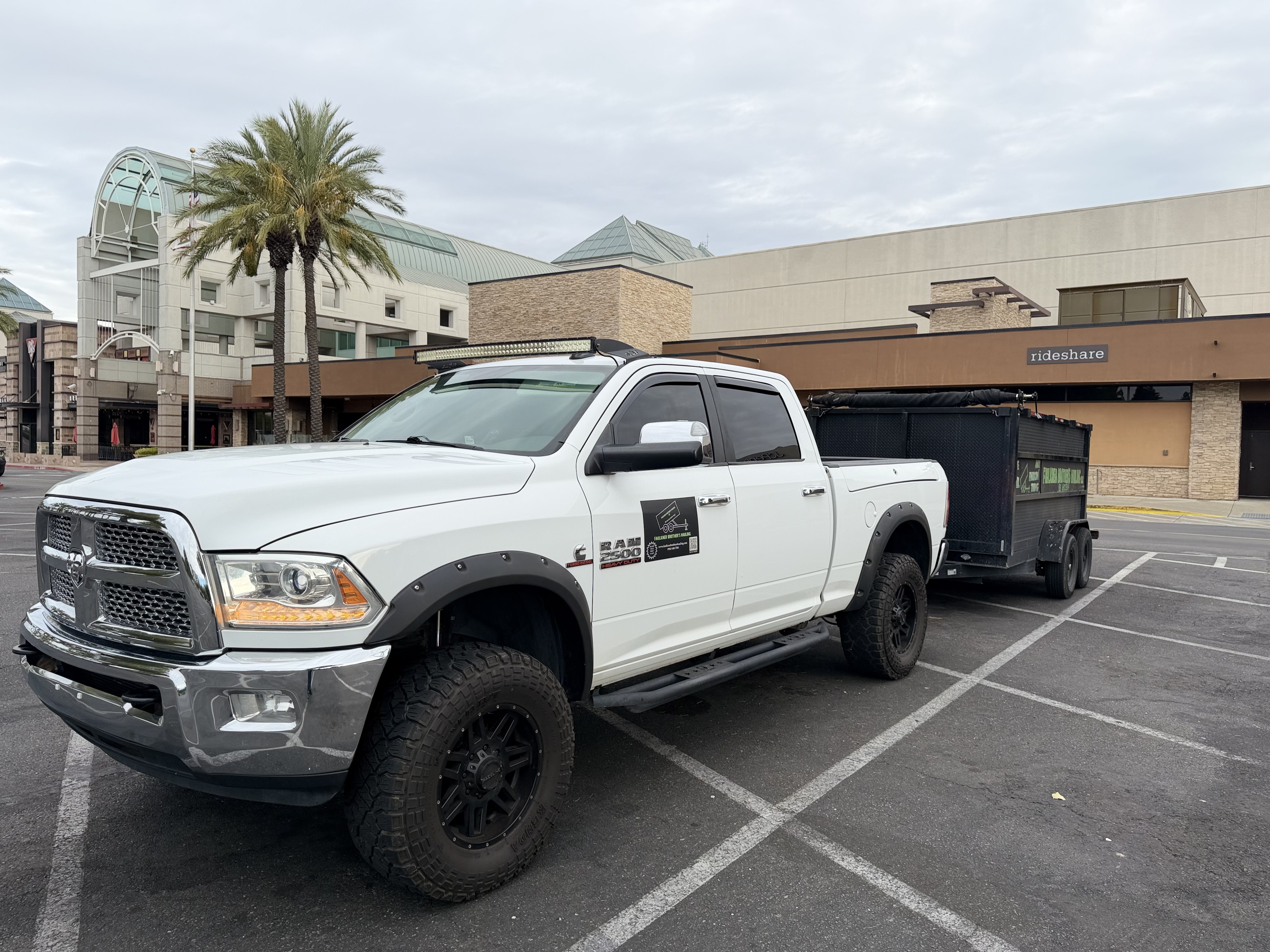 White Faulkner Brothers pickup truck pulling a black dump trailer in a parking lot